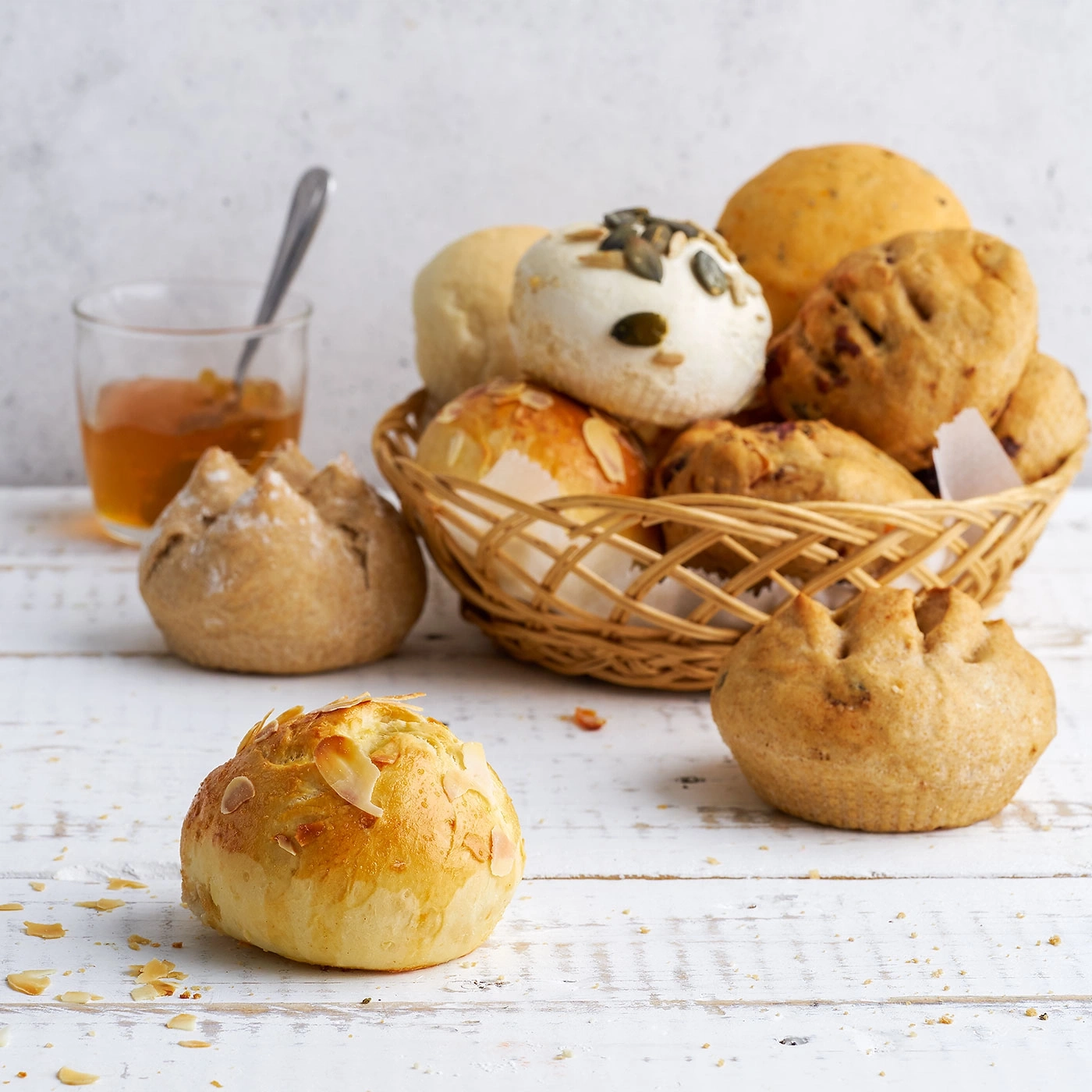 Panier de petits pains, confiture et cuillère sur table blanche