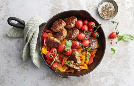 Boulettes de viande frites avec tomates et poivrons dans une poêle avec des herbes