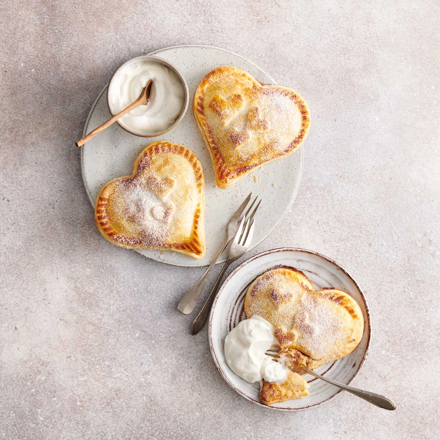 Gâteaux en forme de cœur avec sucre glace et crème sur assiettes avec fourchettes.