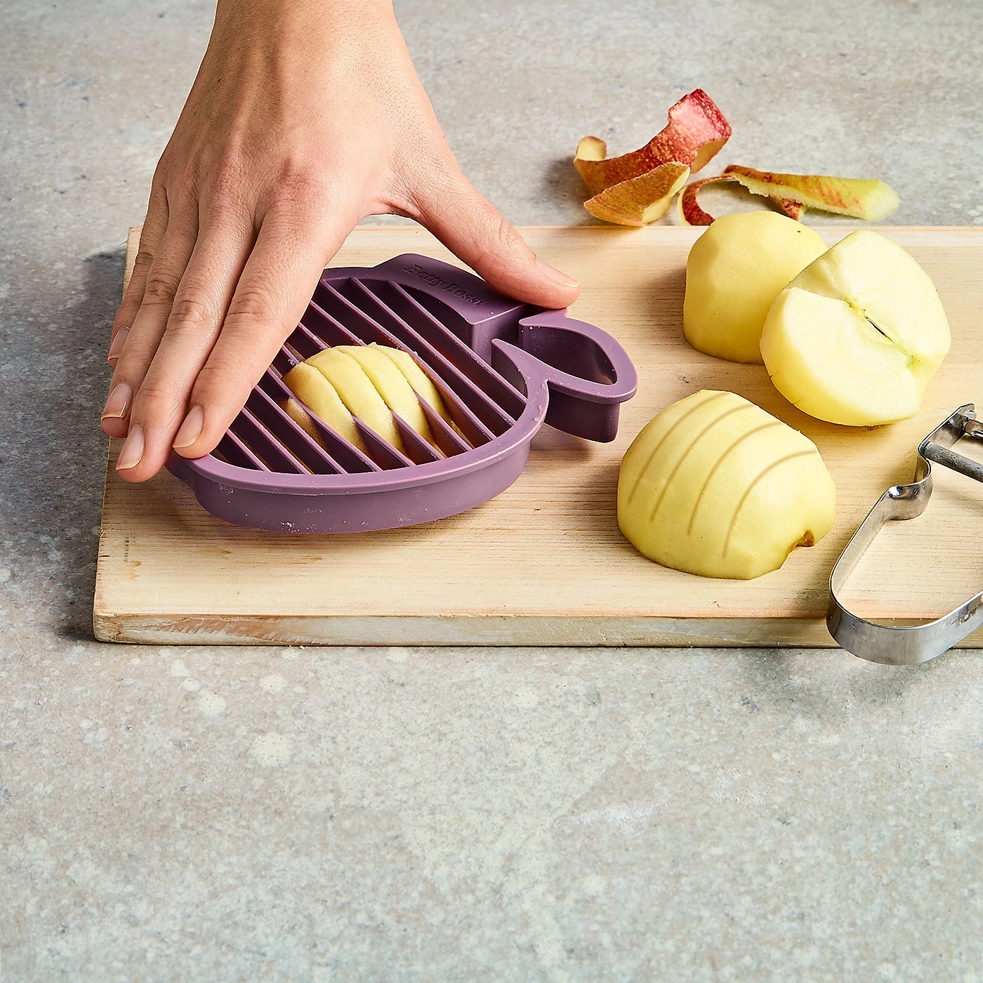 Apfel wird mit einem violetten Apfelschneider auf einem Holzbrett geschnitten.
