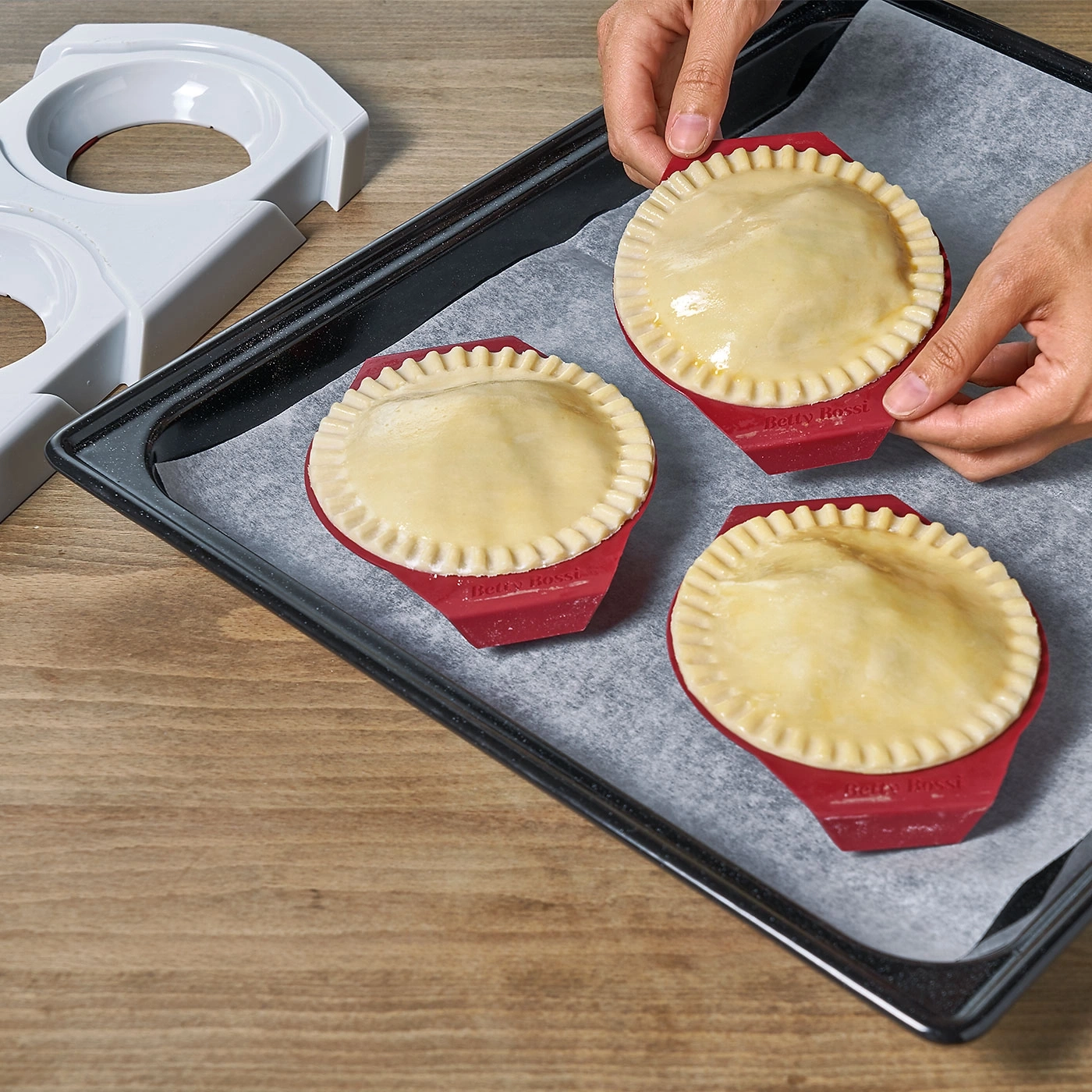 Mains tenant trois tartes sur une plaque à pâtisserie avec du papier sulfurisé.