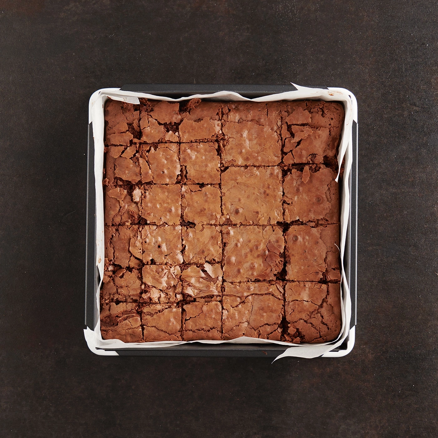 Brownies in einer Backform, quadratisch geschnitten, auf dunklem Hintergrund.