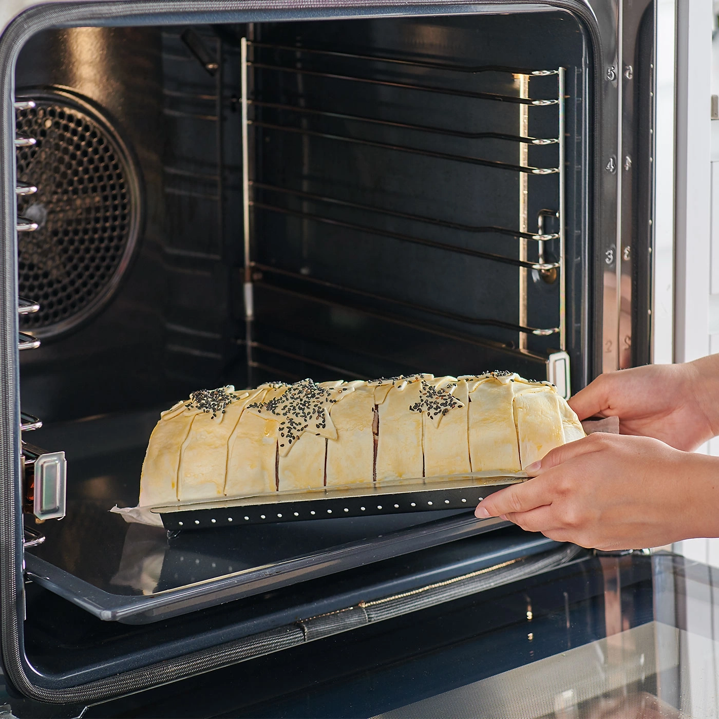 Person legt Gebäck in den Ofen. Backen, Küche, Essen, Teig, Ofen, Hände, Kochen, Lebensmittel, Backblech.