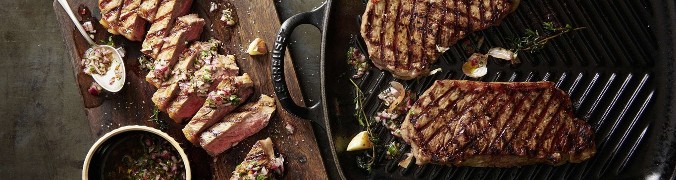 Steak grillé avec salsa sur une planche de bois et une poêle à griller.