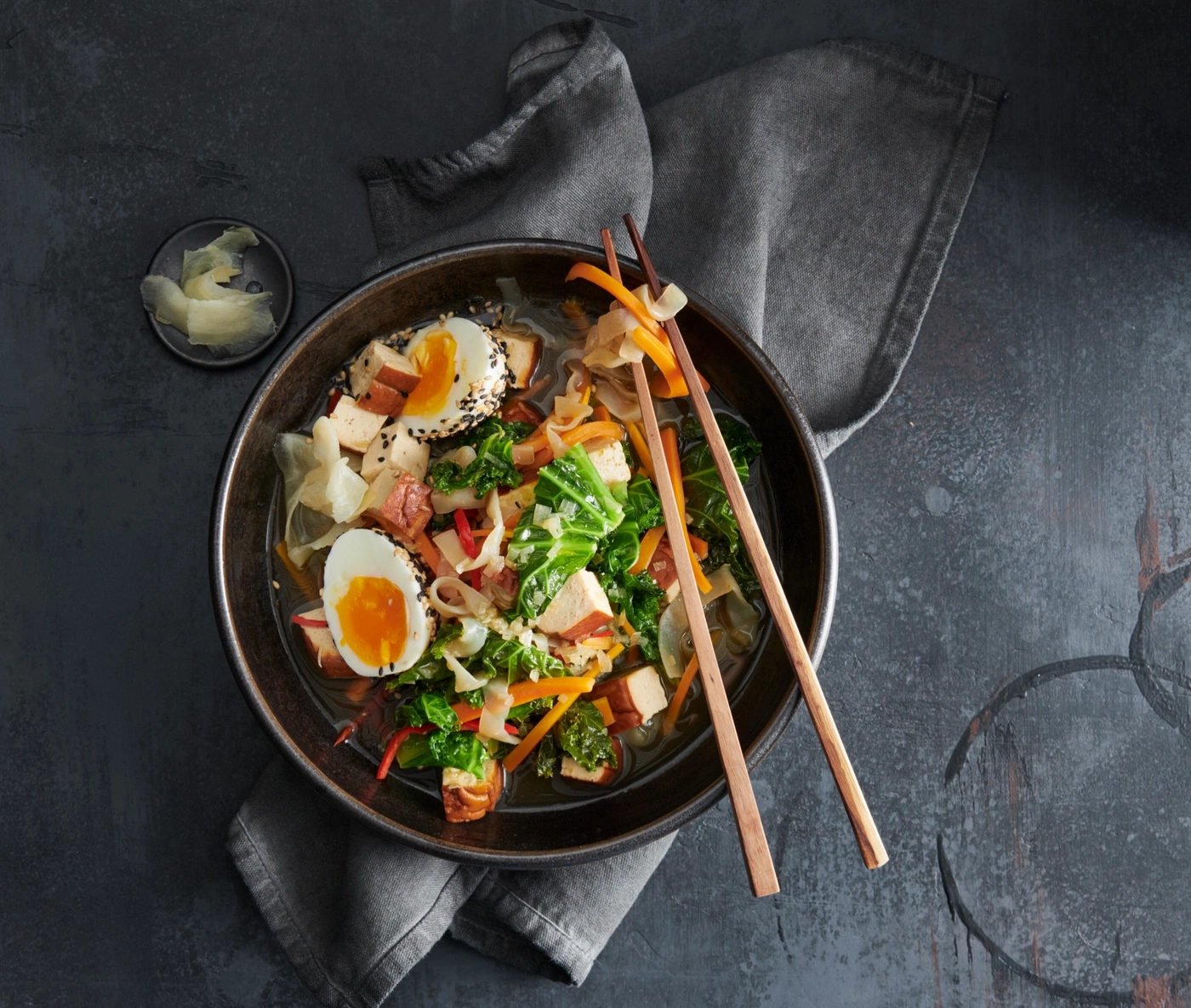Schüssel Ramen mit Gemüse, Ei und Stäbchen auf grauem Hintergrund