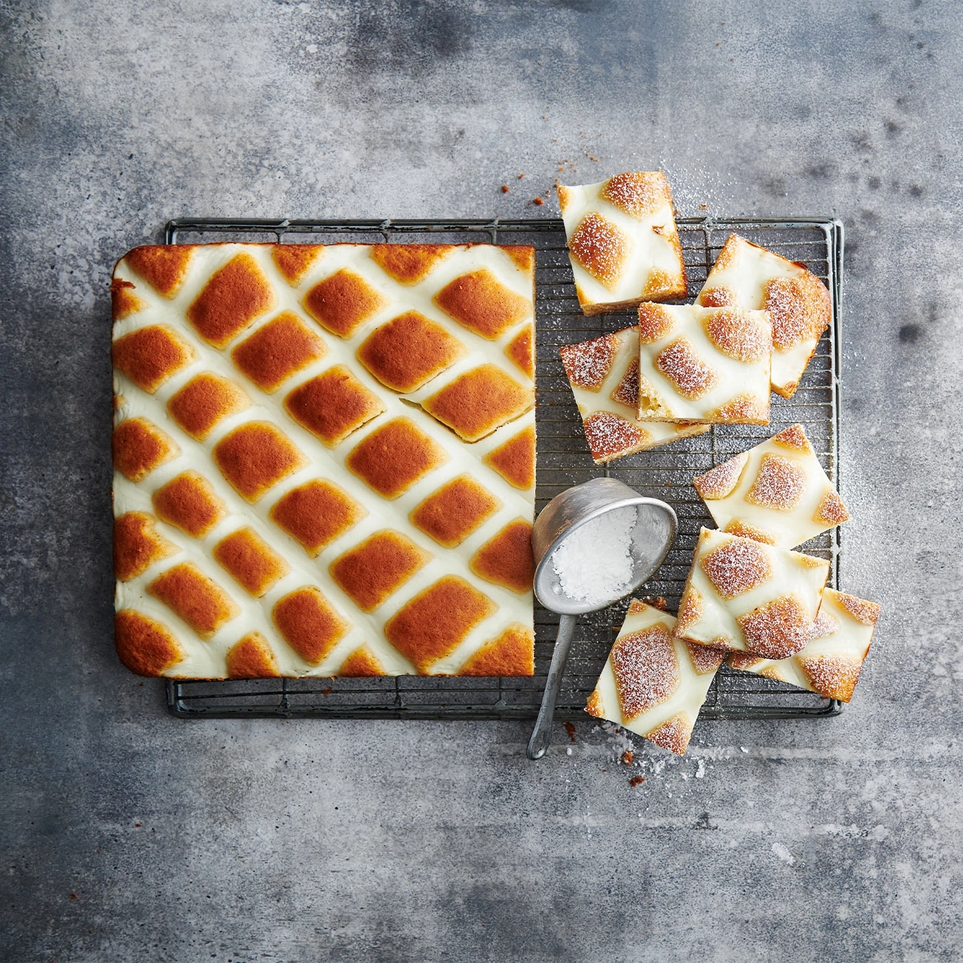Kuchen mit weißer Creme und braunen Quadraten auf einem Rost, Zuckerstreuer