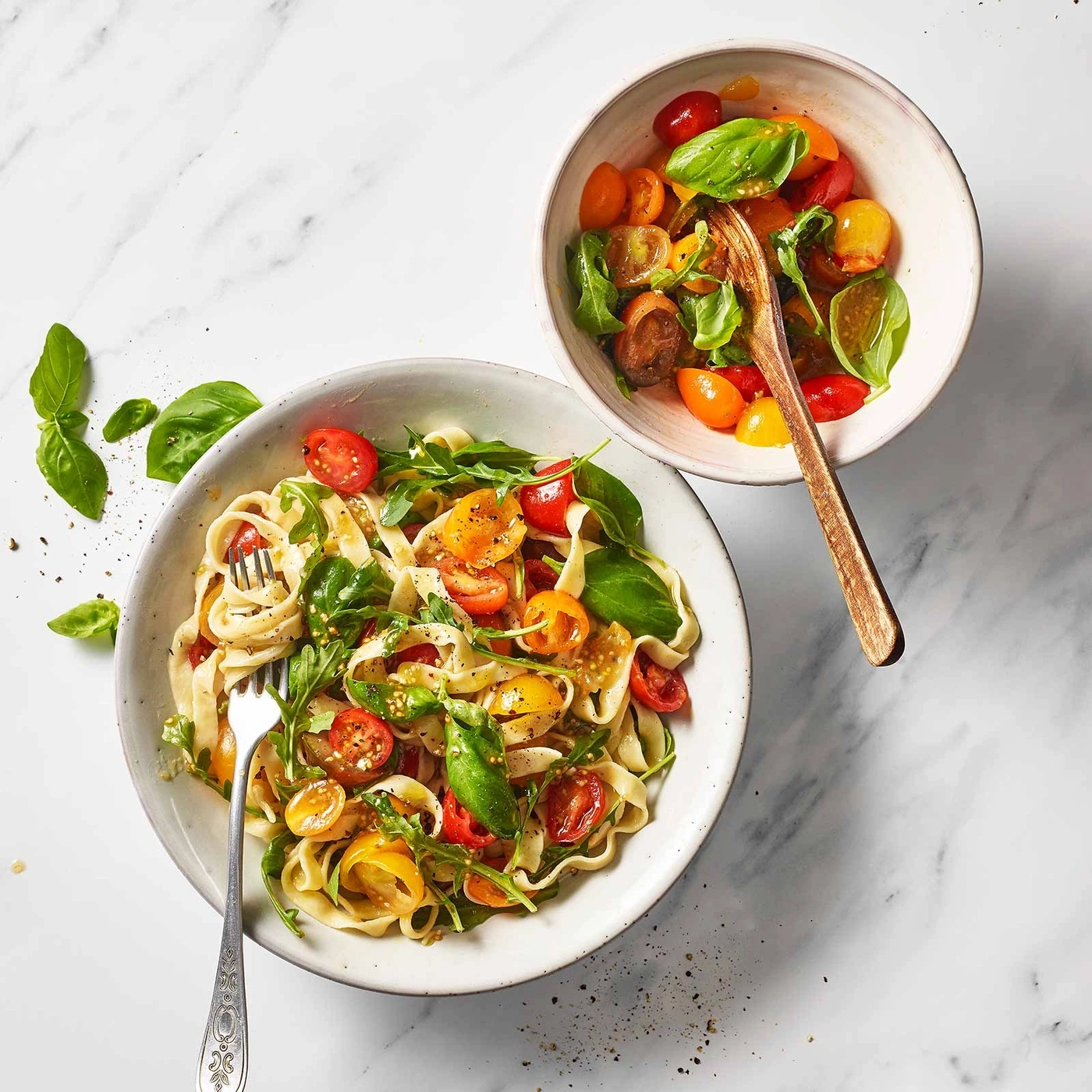 Pasta mit Tomaten und Basilikum in Schalen auf Marmorplatte