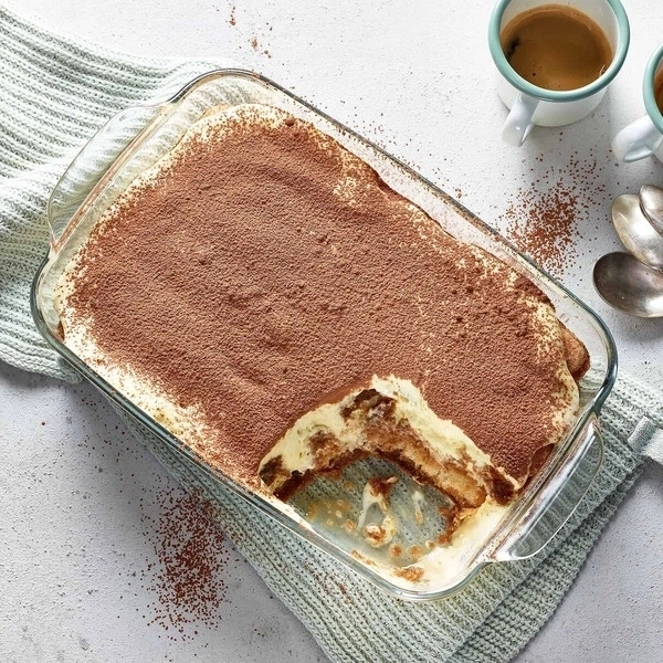 Tiramisu in Glasform, Kaffeetassen und Löffel auf dem Tisch