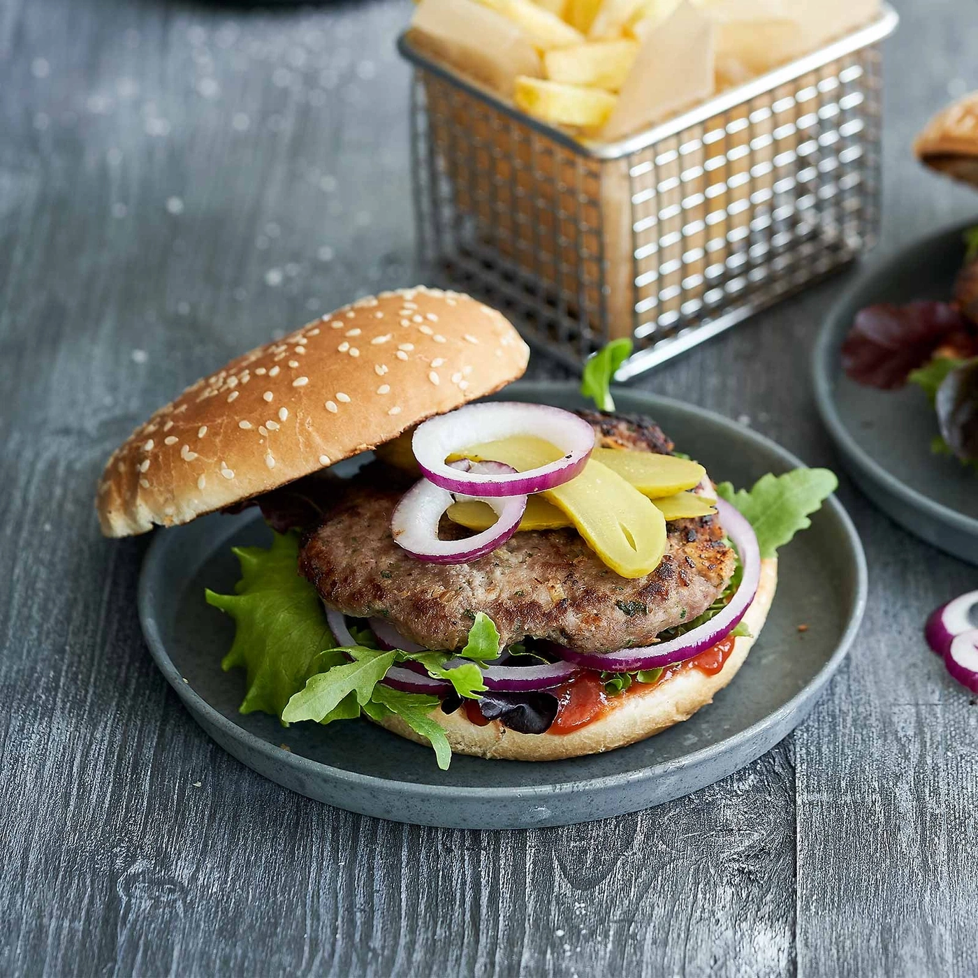 Burger mit Zwiebeln, Gurken und Pommes Frites auf einem grauen Teller