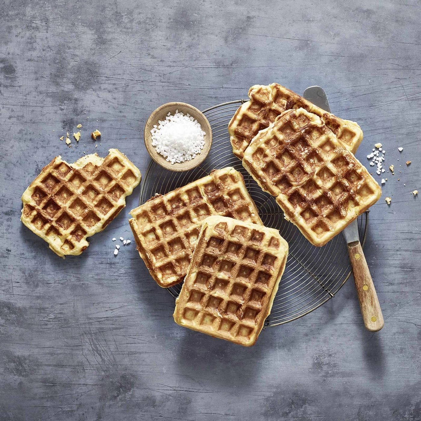 Waffeln auf einem Rost mit Zuckerstreusel und einem Messer auf grauem Hintergrund.