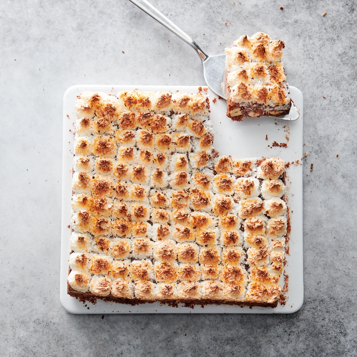 Kuchen mit Kokosnuss-Topping auf weißem Tablett, ein Stück wird serviert.