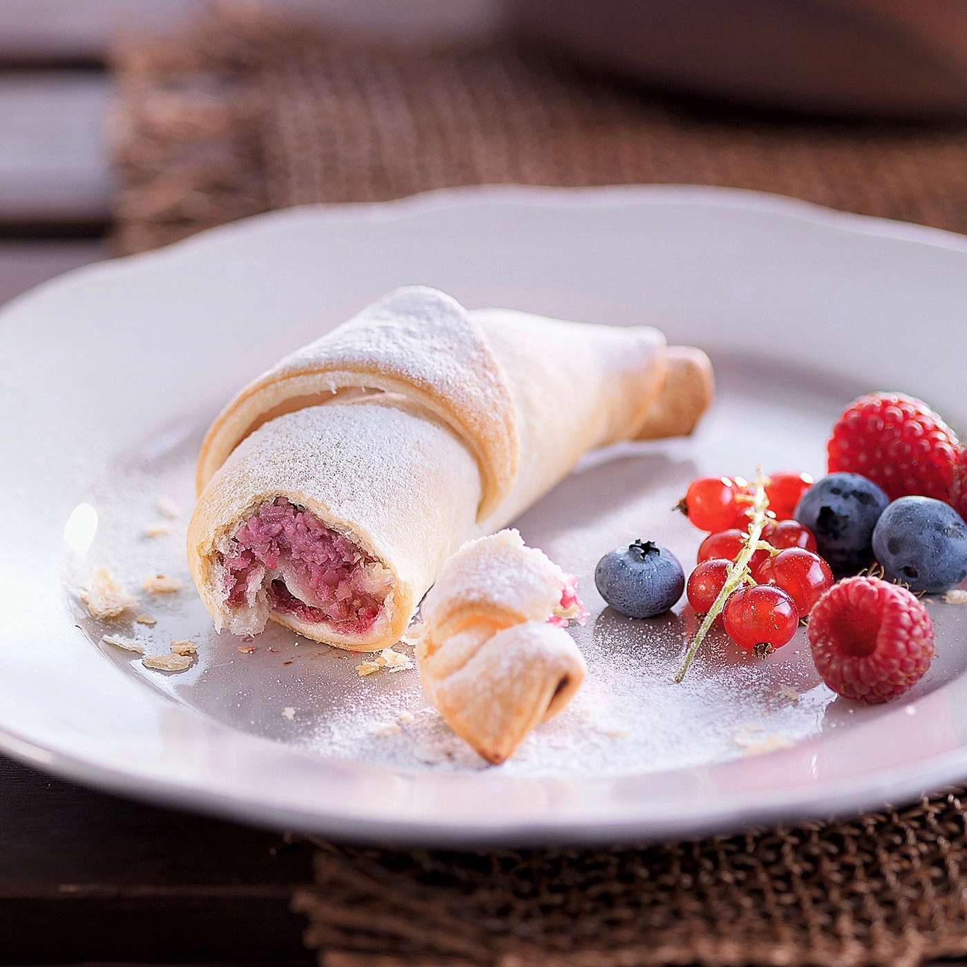 Croissant mit Beeren auf einem Teller, mit Puderzucker bestäubt.