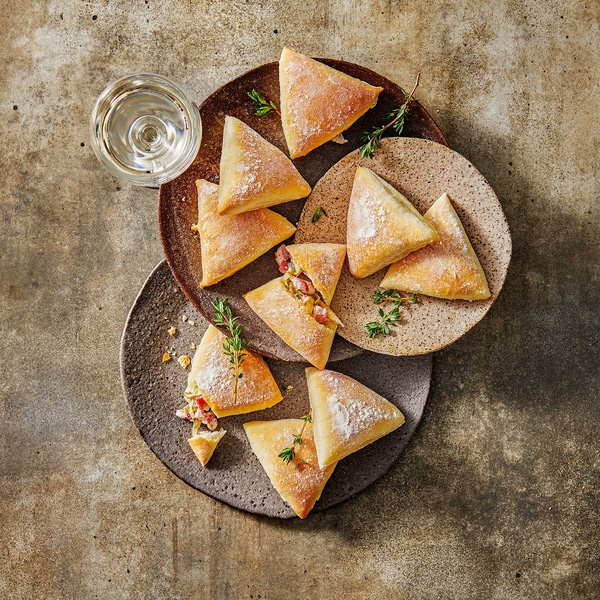 Des chaussons triangulaires sur des assiettes avec un verre de vin sur une table