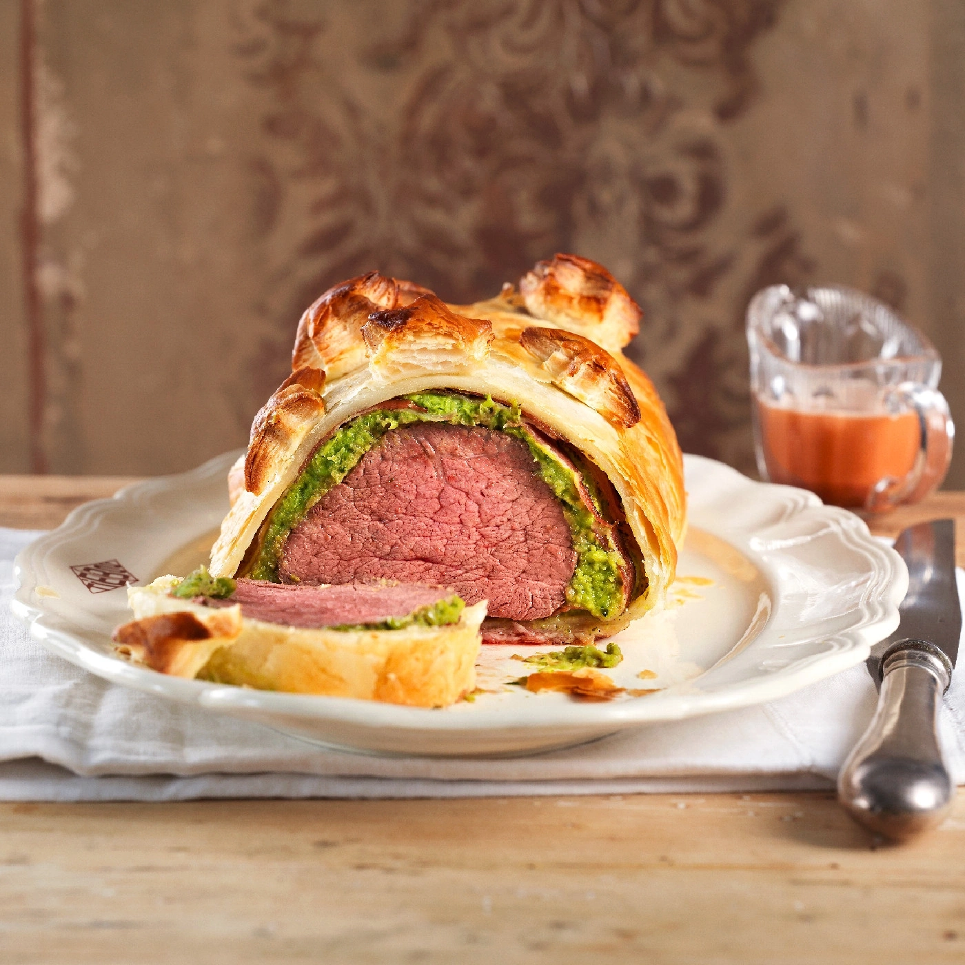 Rindfleisch Wellington, auf einem Teller serviert, mit Soße und Messer.