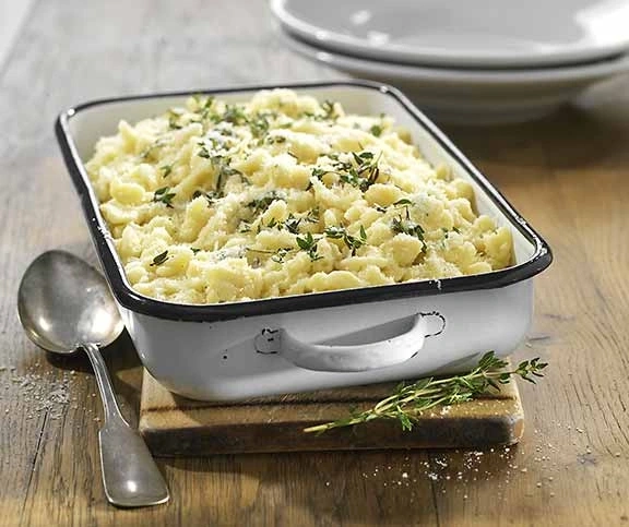 Käsespätzle in einer Auflaufform mit Kräutern und Löffel auf Holz
