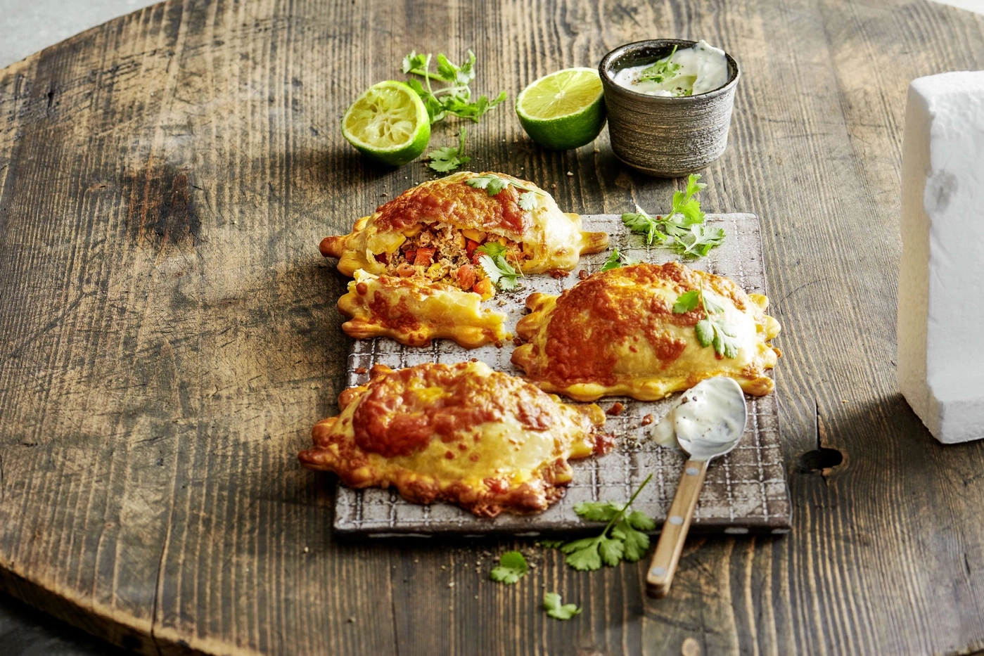 Empanadas auf Holzbrett mit Limetten, Kräutern und Dip. Rustikal.
