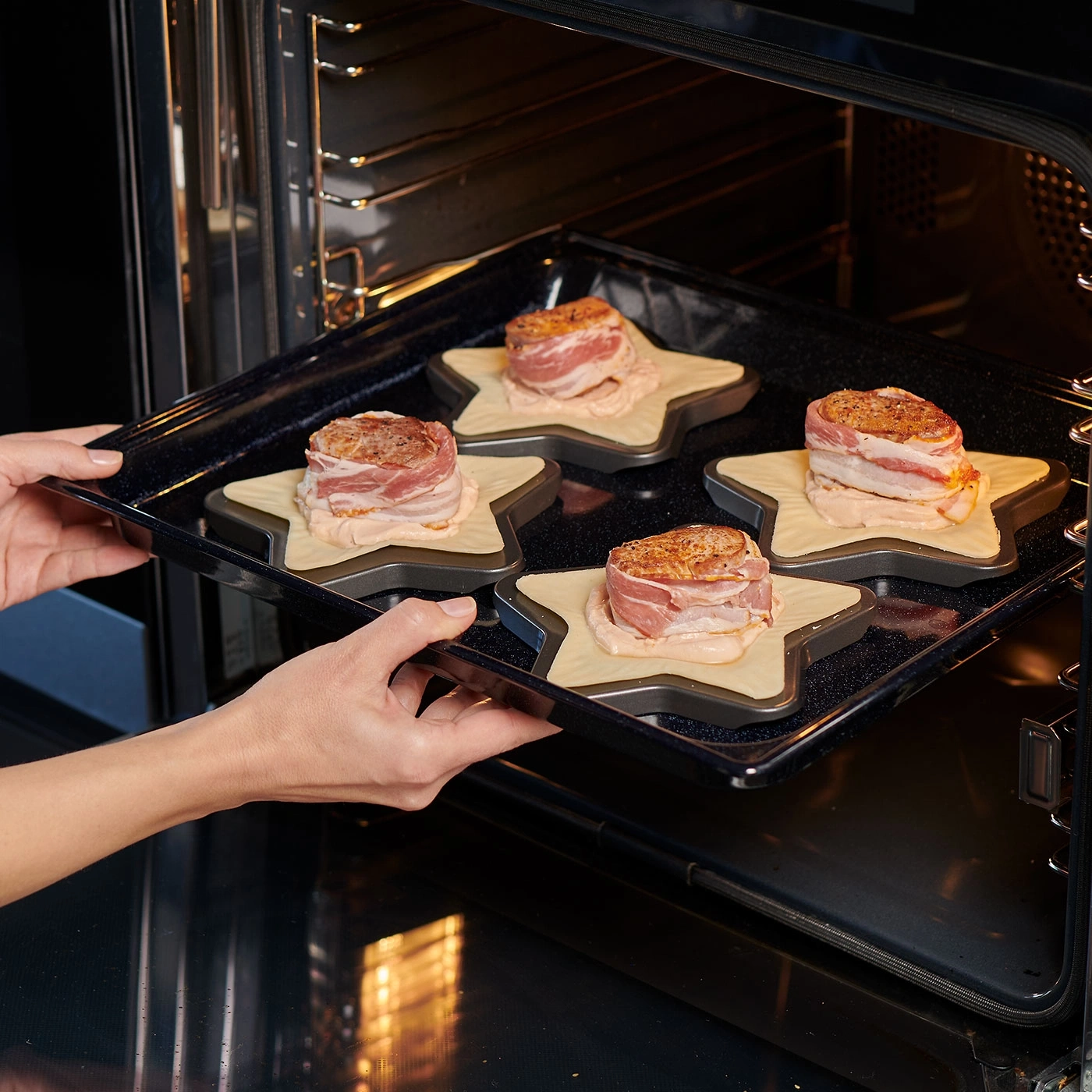 Personne place une plaque de cuisson avec de la viande au four. Formes d'étoiles, bacon.