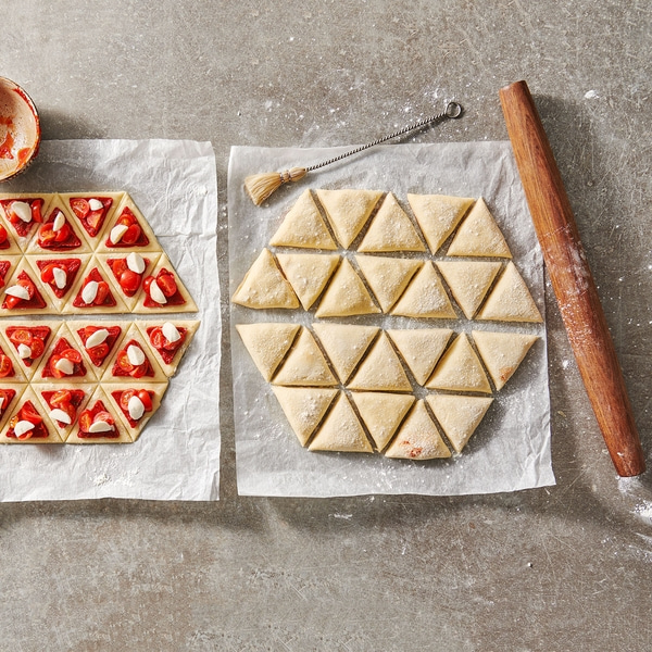 Des triangles de pizza sur papier sulfurisé, pâte et rouleau à pâtisserie.