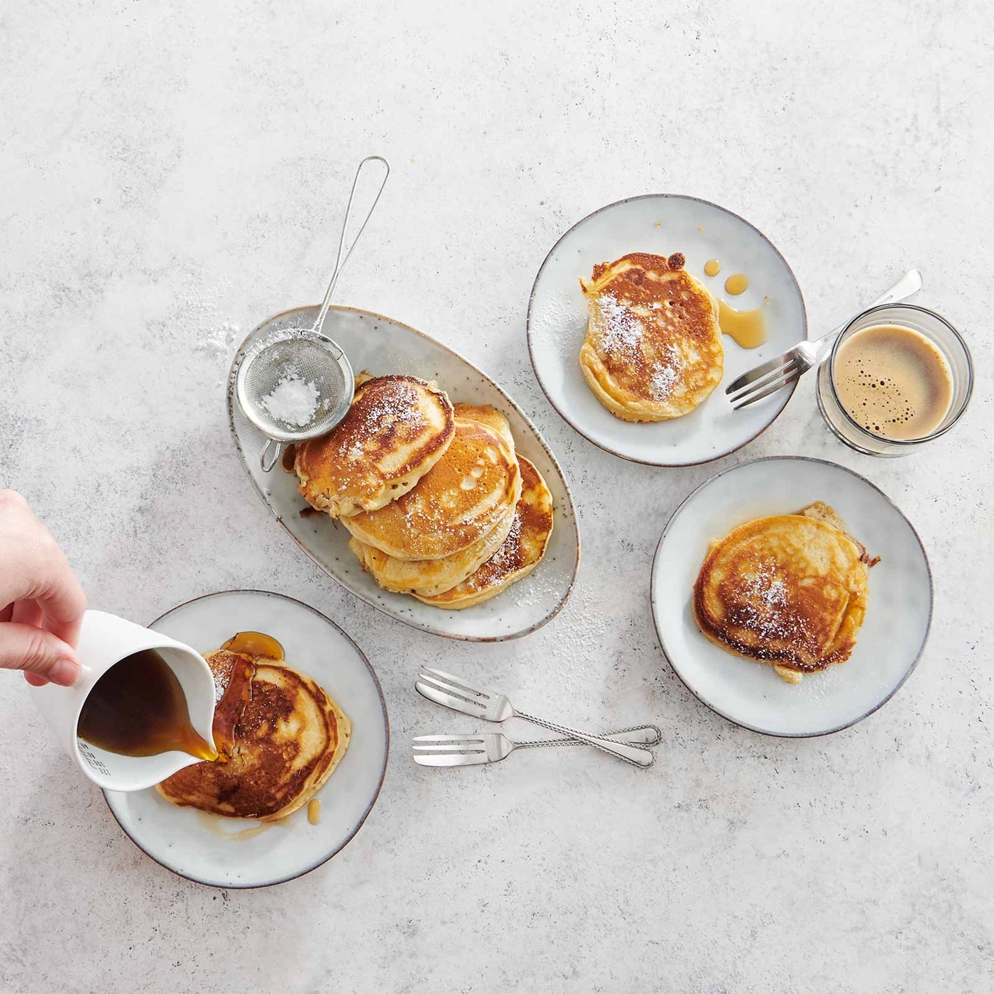 Pfannkuchen mit Puderzucker und Sirup, serviert mit Kaffee und Gabeln.