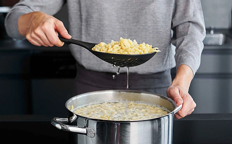 Person kocht Spätzle, die aus dem Topf mit einem Schaumlöffel genommen werden.