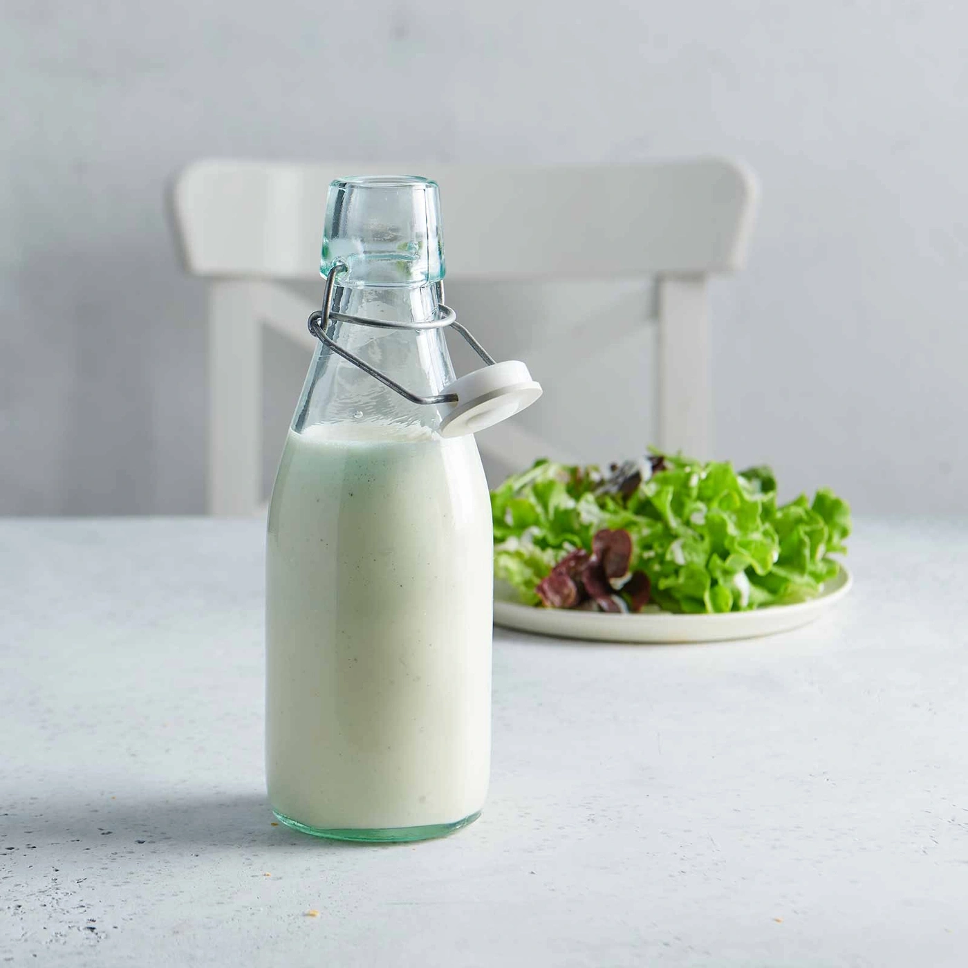 Salatdressing in einer Flasche mit Salat auf einem Teller und einem Stuhl im Hintergrund.