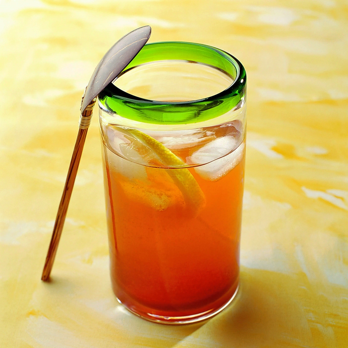 Glas mit Getränk, Eis, Zitrone und Löffel auf gelbem Hintergrund.