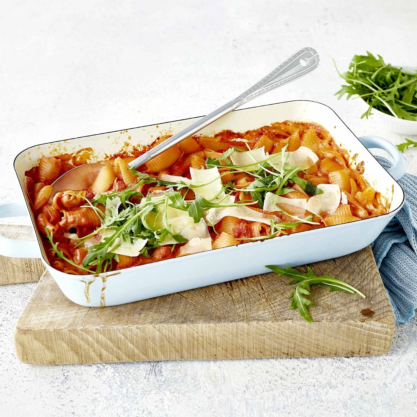 Pasta-Auflauf mit Rucola und Parmesan auf Holzbrett serviert