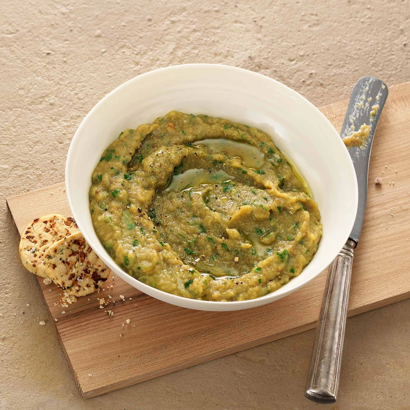 Auberginen-Dip in einer Schüssel mit Brot und Messer auf Holzbrett