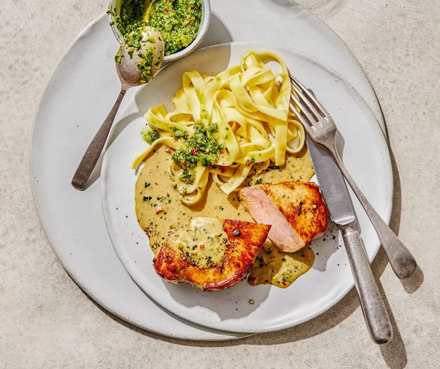 Une assiette de filet de porc avec des pâtes tagliatelles et une sauce verte.