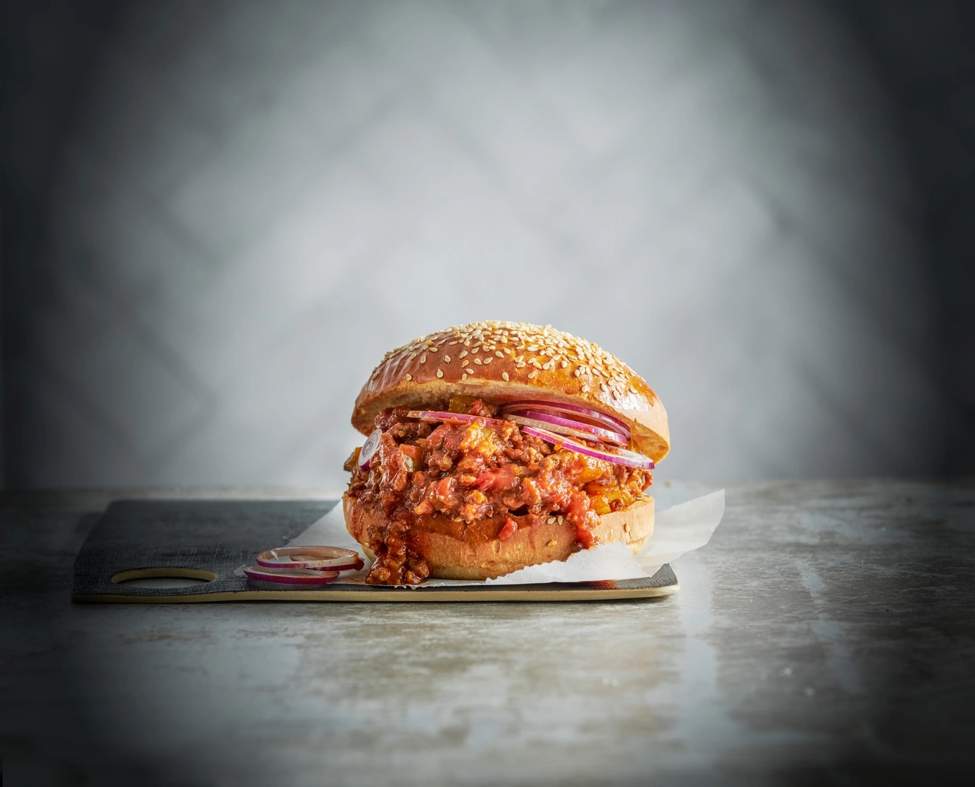 Ein köstlicher Burger mit Fleisch, Zwiebeln und Brötchen auf einem Brett.