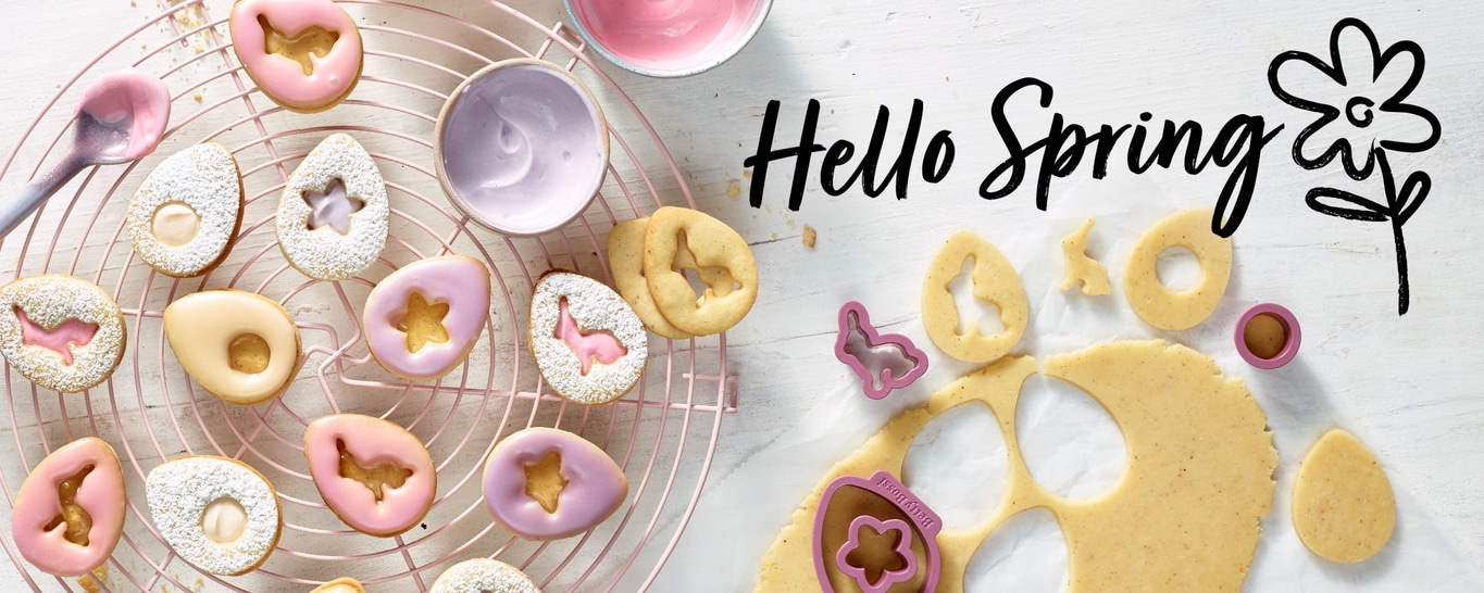 Osterkekse mit Zuckerguss und Ausstechern auf einem Gitter, 'Hello Spring'.