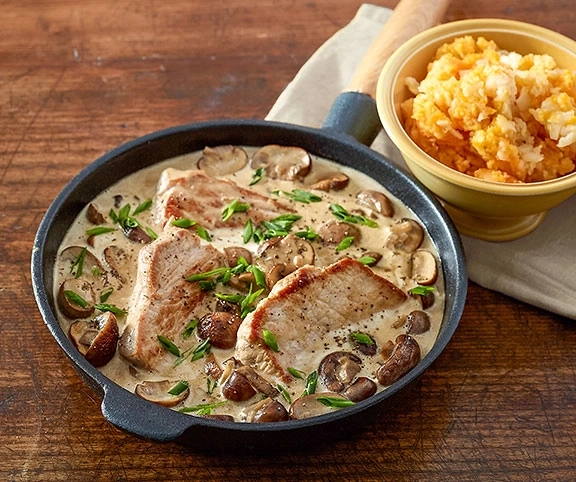 Schweinekotelett mit Pilzen und Kartoffelpüree, serviert in einer Pfanne.