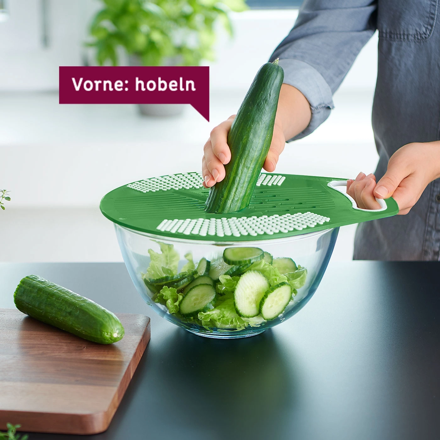 Person schneidet Gurke mit Küchengerät in einer Glasschüssel mit Salat.