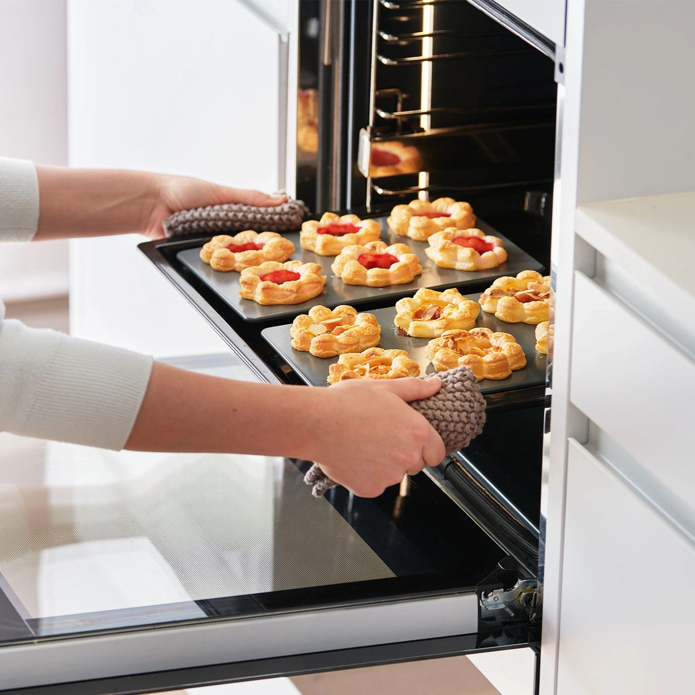 Person nimmt Backblech mit Gebäck aus dem Ofen. Küche, Backen, Essen.