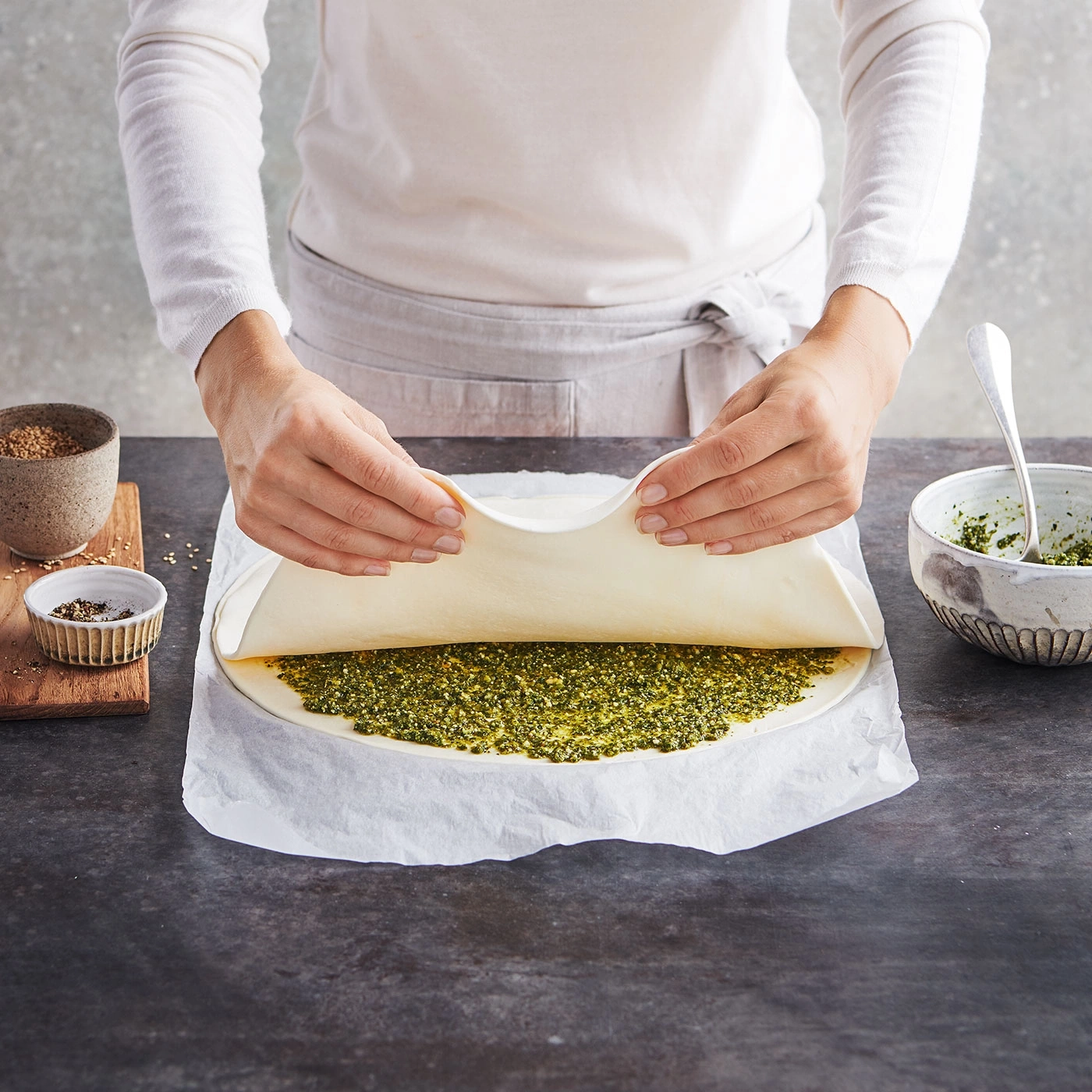 Personne pliant la pâte sur une garniture verte. Cuisine, préparation culinaire, repas.