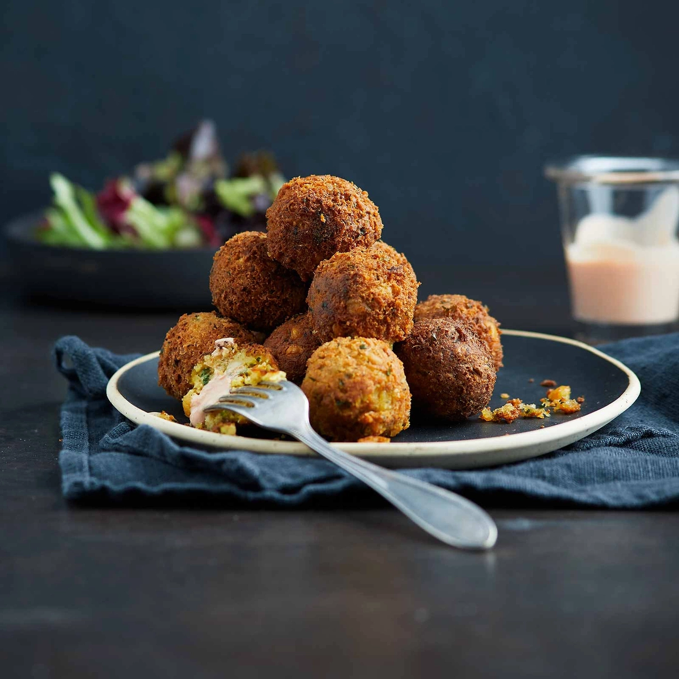 Falafel-Bällchen auf einem Teller mit Soße und Salat, Nahaufnahme.