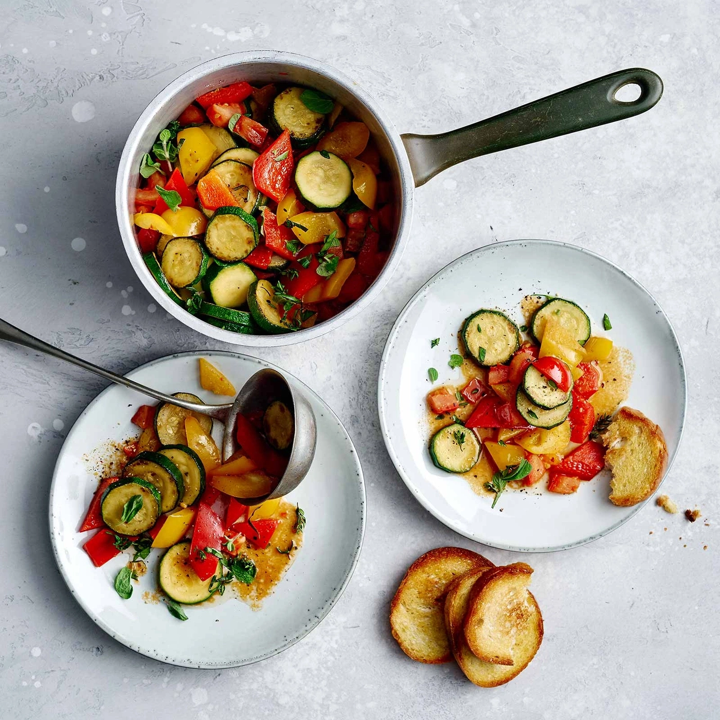 Gemüsegericht mit Zucchini, Paprika, Tomaten und Brot auf Tellern und in einem Topf
