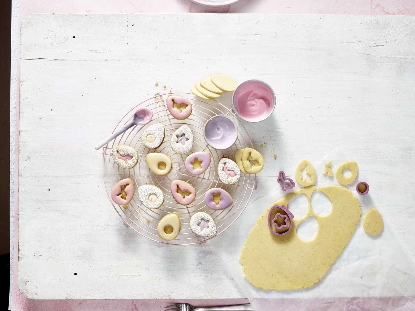 Osterkekse auf einem Gitter, mit Zuckerguss und Ausstechern auf einem Tisch