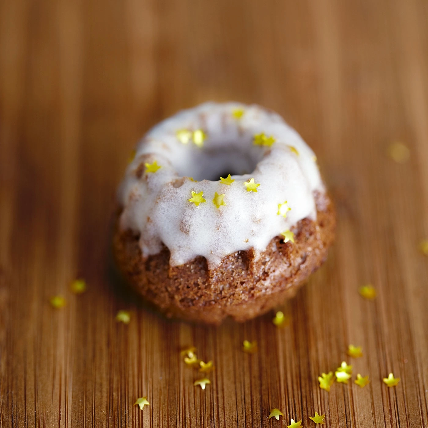 Petit gâteau avec glaçage et étoiles dorées sur fond en bois.