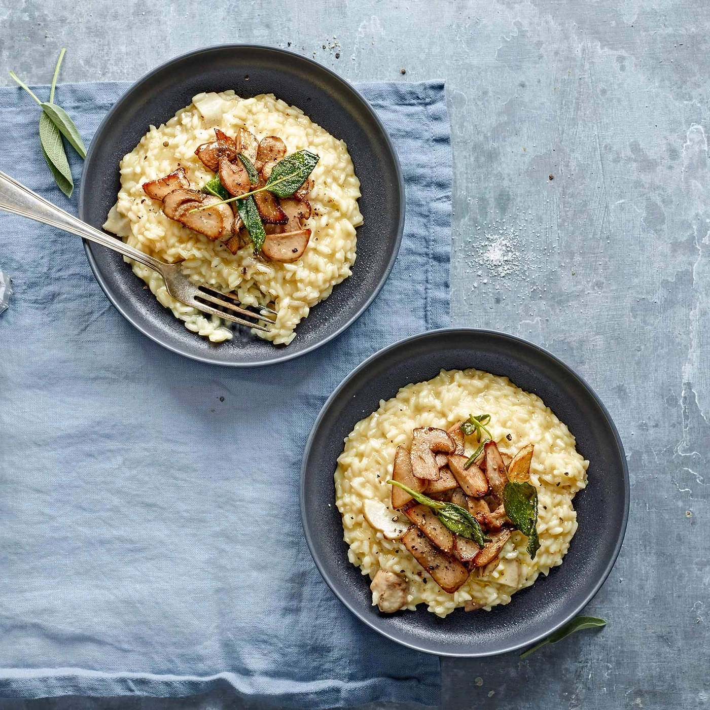 Zwei Teller Risotto mit Pilzen und Salbei auf blauem Tuch