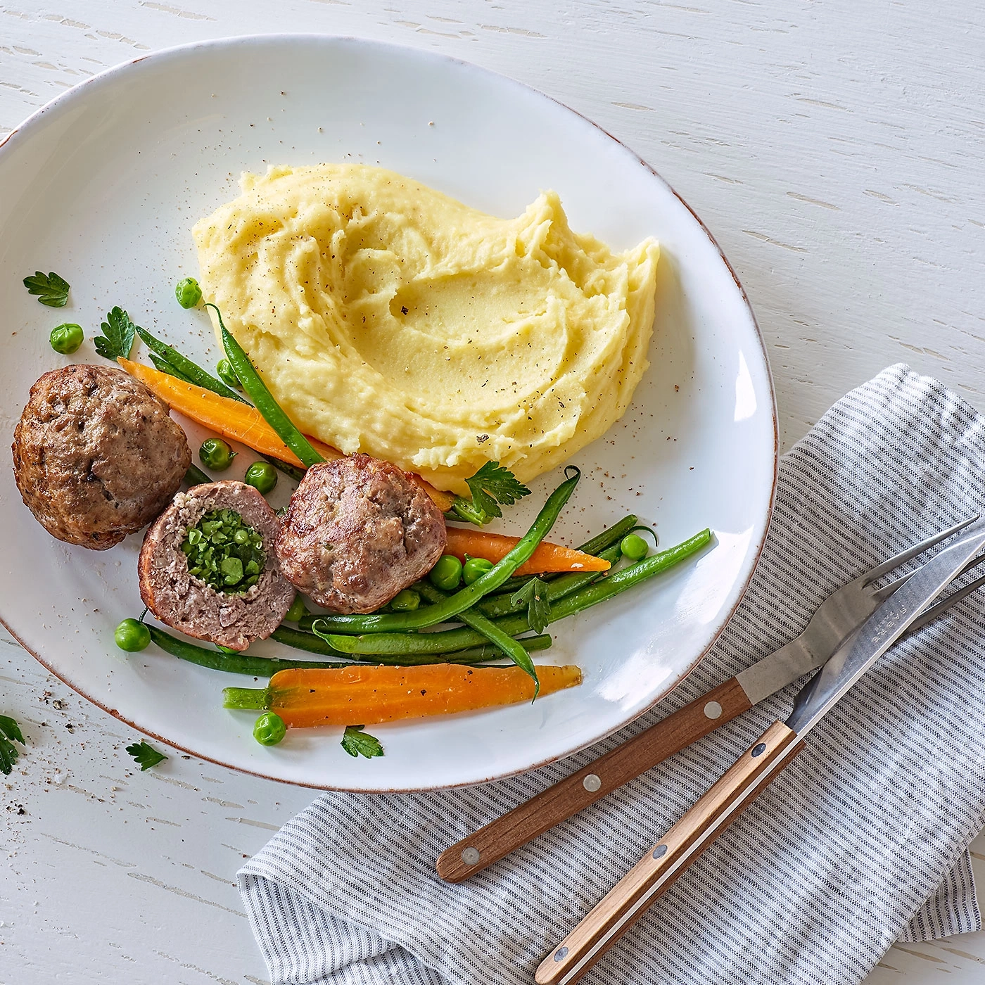 Teller mit Fleischbällchen, Kartoffelpüree und Gemüse, serviert mit Besteck.