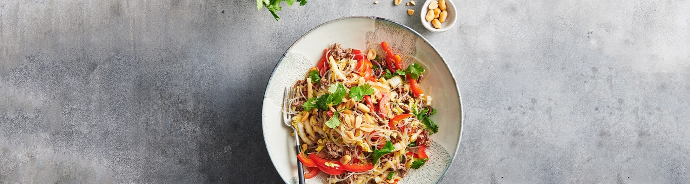 Asiatisches Gericht mit Nudeln, Gemüse, Fleisch und Erdnüssen auf einem Teller