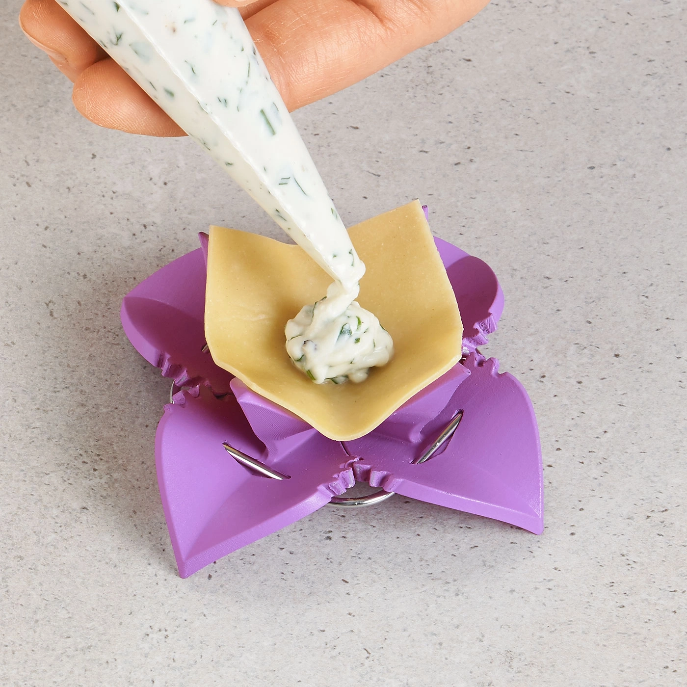 Person füllt Ravioli mit Creme. Lila Ravioli-Former und Teigblatt.