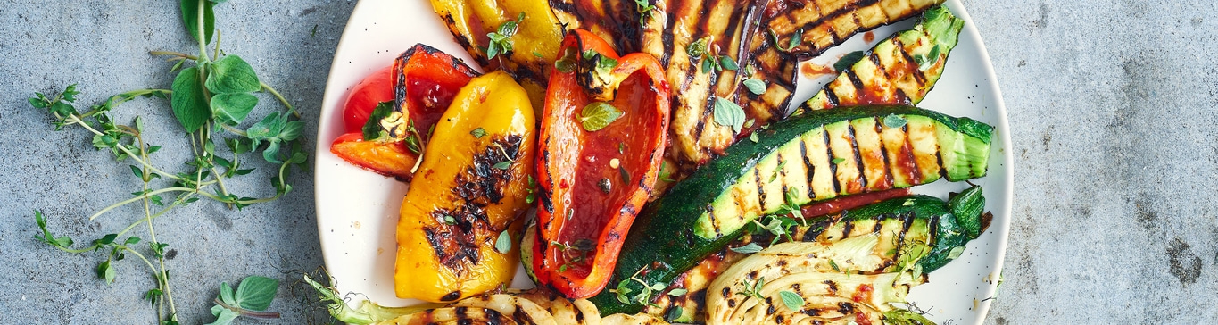 Gegrilltes Gemüse auf einem Teller mit Kräutern, Paprika, Zucchini und Tomaten