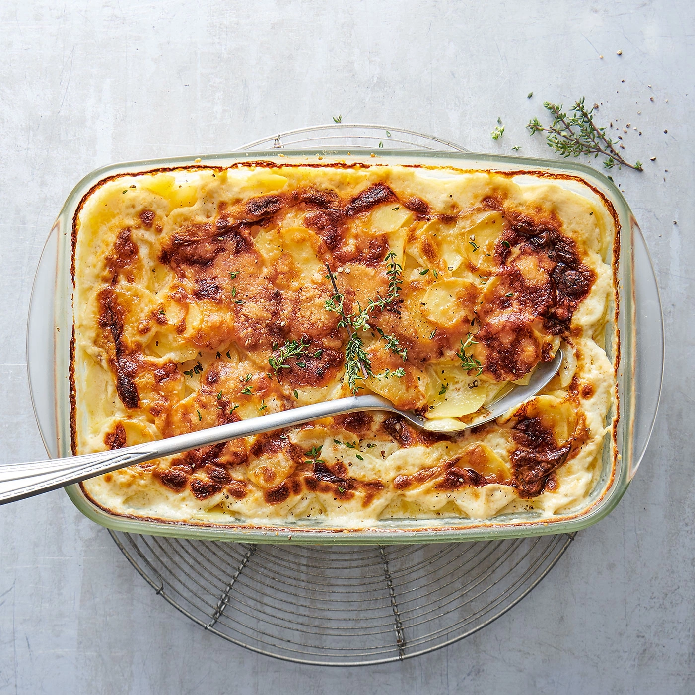 Auflauf mit Kartoffeln und Käse, serviert in einer Glasform mit Kräutern.