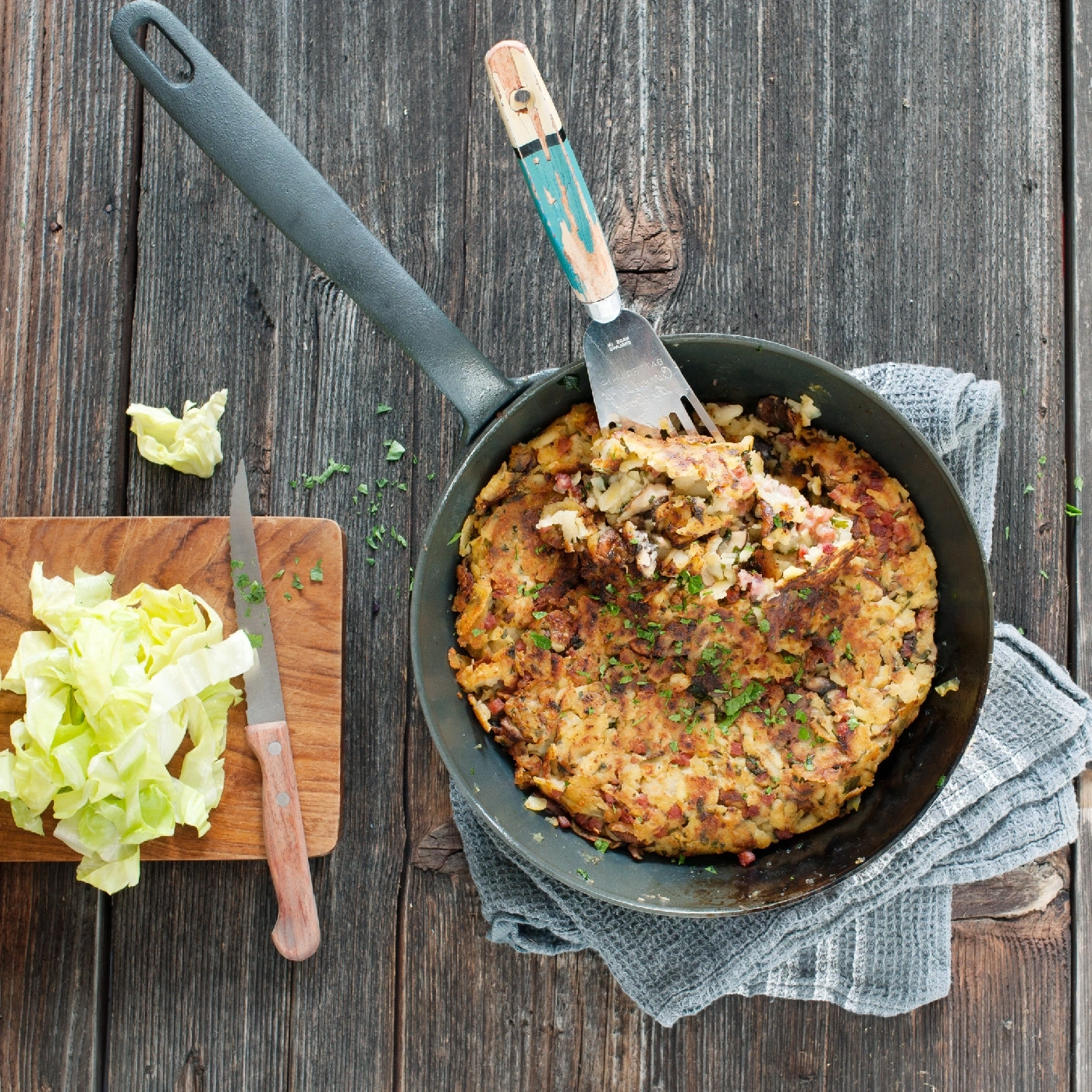 Pfannkuchen in der Pfanne mit Salat und Messer auf Holzbrett