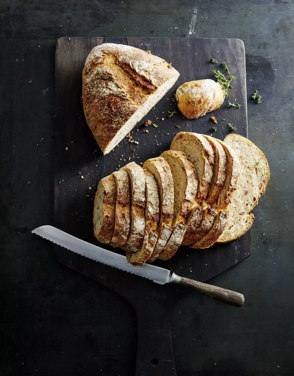 Ein angeschnittenes Brot mit einer Scheibe und einem Messer auf einem Holzbrett.