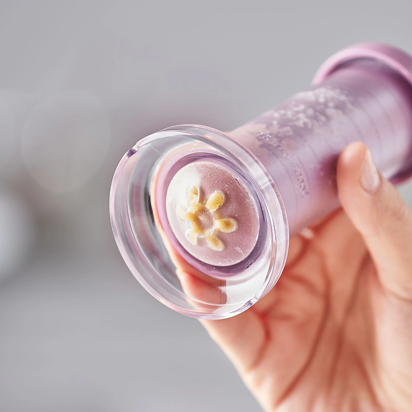 Gros plan d'un outil violet avec un motif floral, tenu par une main, sur fond clair.