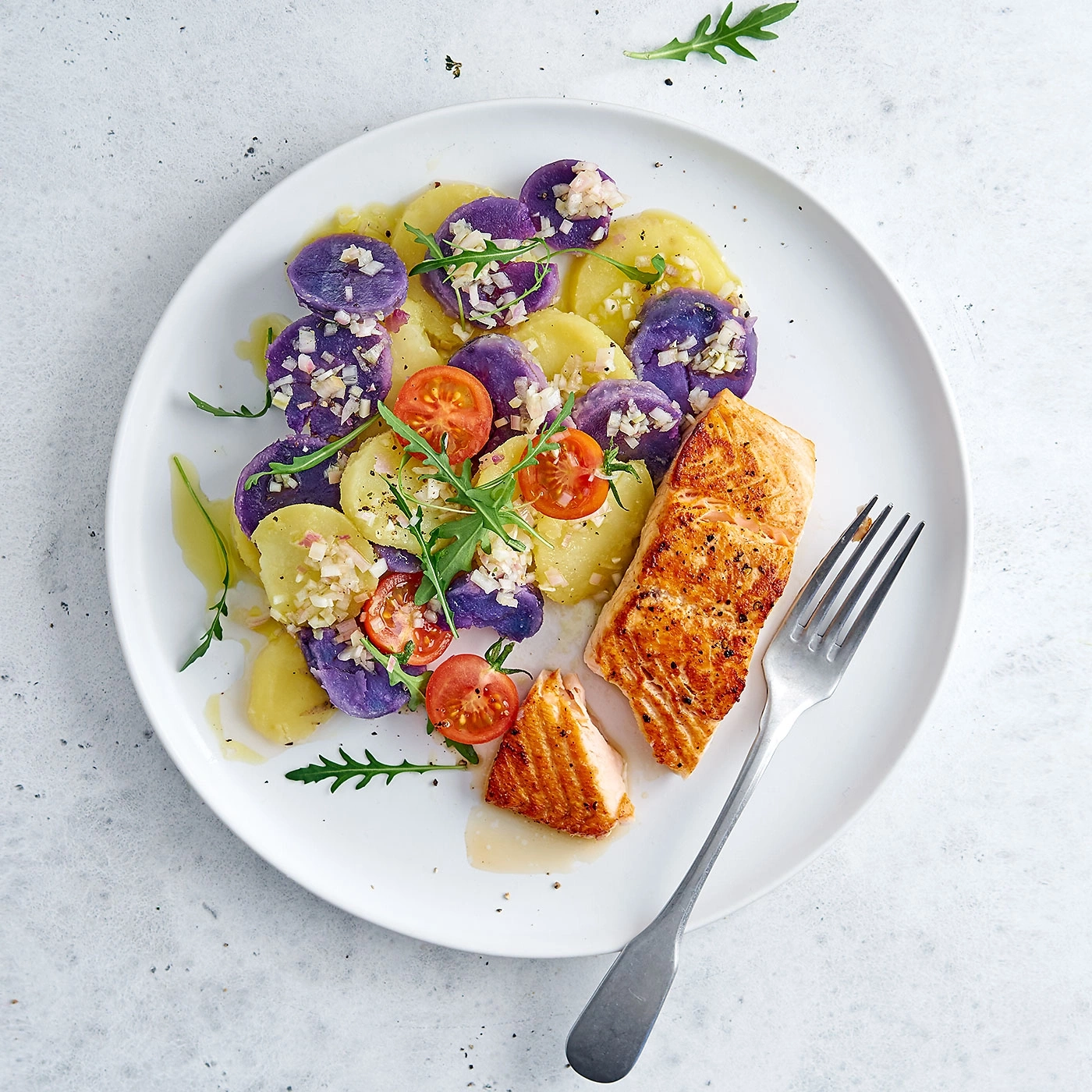 Lachs mit Kartoffelsalat und Tomaten auf einem weißen Teller