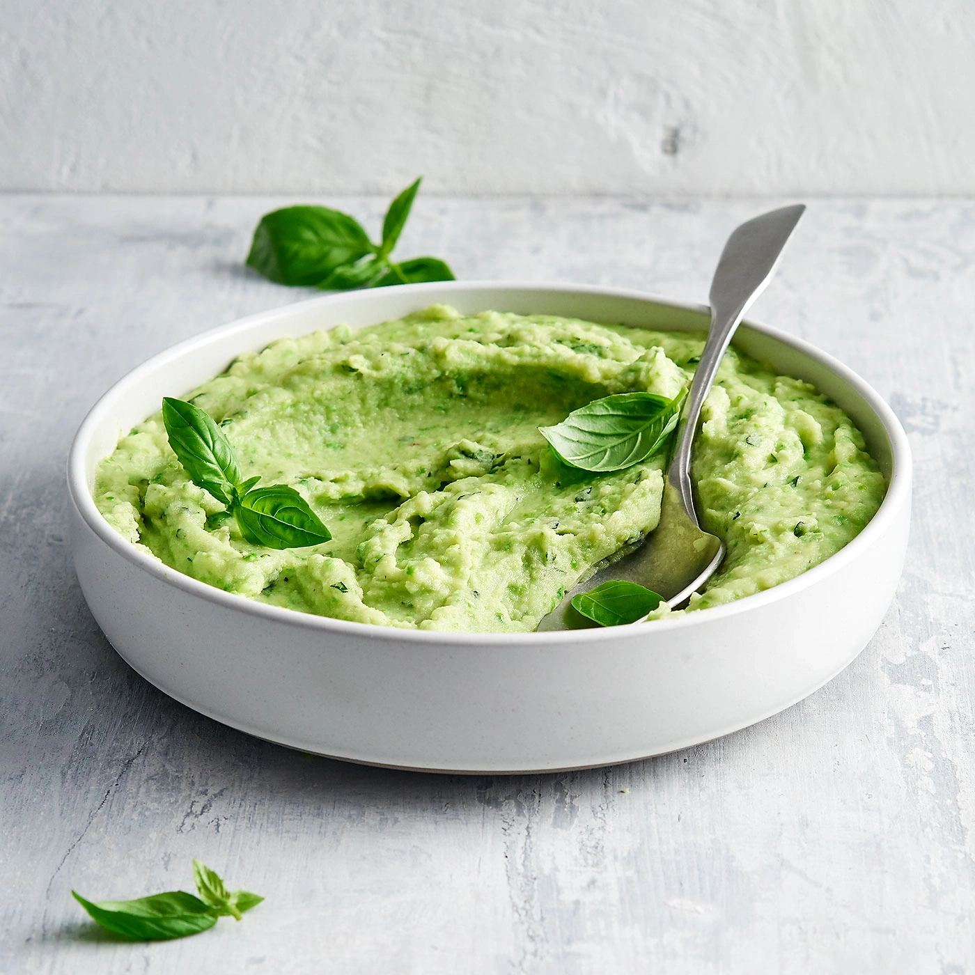 Purée verte avec du basilic dans un bol blanc avec une cuillère.